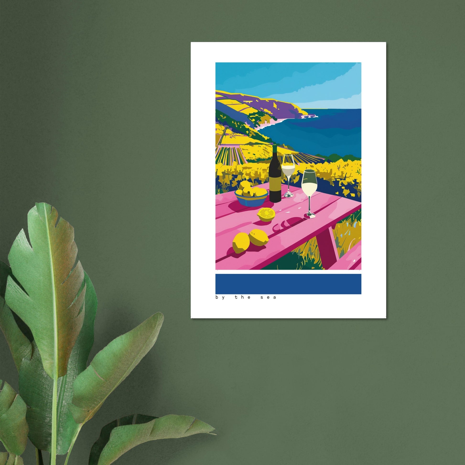 Framed By the Sea artwork displayed in a bright living room, featuring a coastal picnic table with wine, lemons, and vivid blue sea cliffs. Soft natural light enhances the bold Mediterranean colours. The framed print adds warmth, freshness, and coastal charm, making it ideal for kitchens, dining rooms, or relaxed holiday-style interiors.